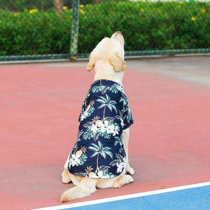 Labrador dog wearing blue Hawaiian shirt with palm tree and floral print sitting on outdoor court