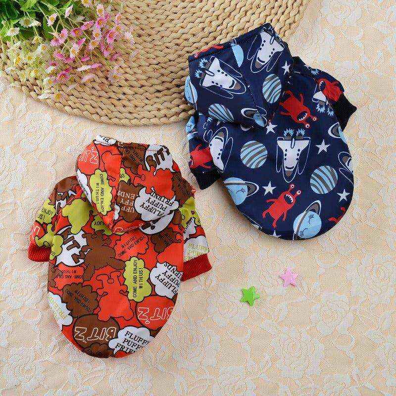 Two colorful fleece-lined dog hoodies with cartoon prints on a lace tablecloth with flowers and star decorations
