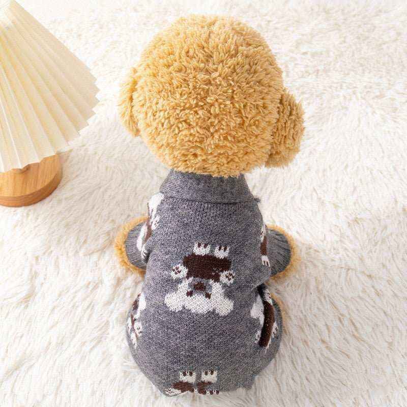 Small dog wearing gray sweater with teddy bear pattern sitting on white fluffy rug next to wooden lamp