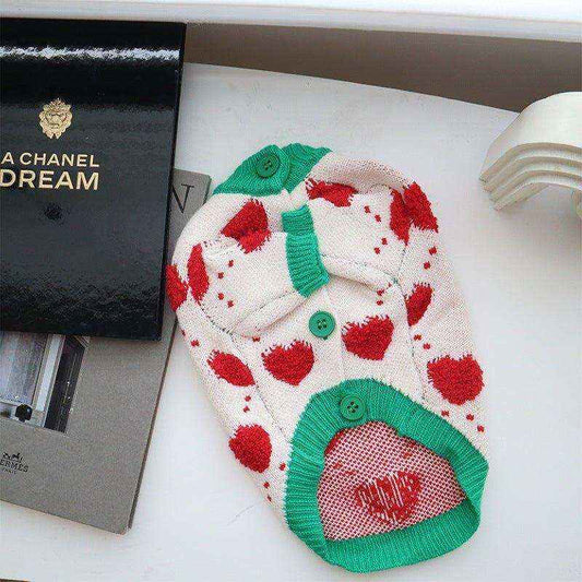 Knitted dog cardigan with red heart pattern and green trim, laid on white surface with books nearby