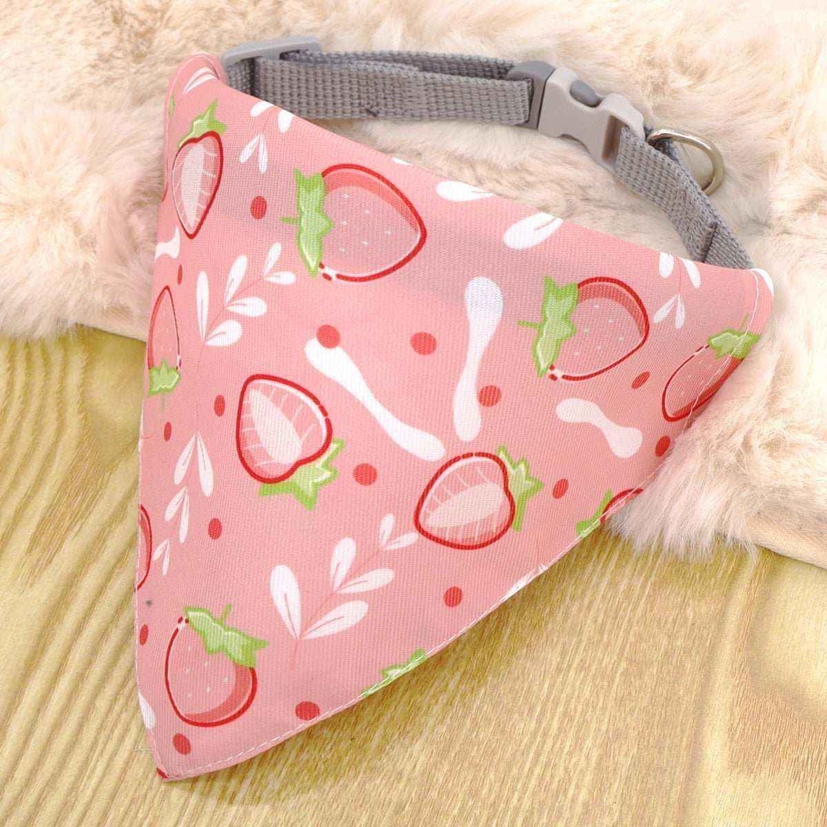 Pink dog bandana with strawberry and white bone patterns attached to gray nylon collar on wooden surface