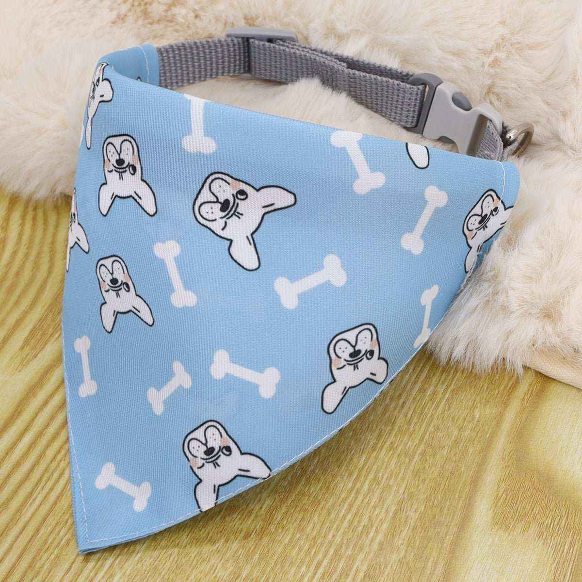 Blue dog bandana with white bone and dog face patterns attached to gray nylon collar on wooden surface