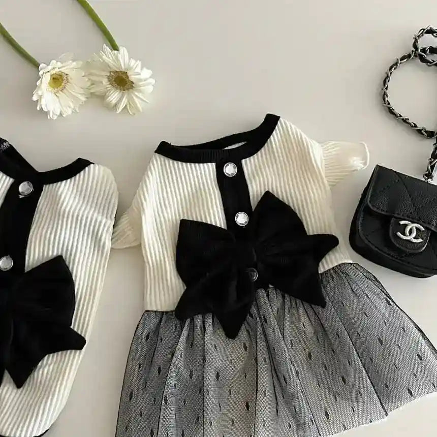 Elegant baby dress with black bow and buttons, sheer black skirt, white daisies, and small black purse