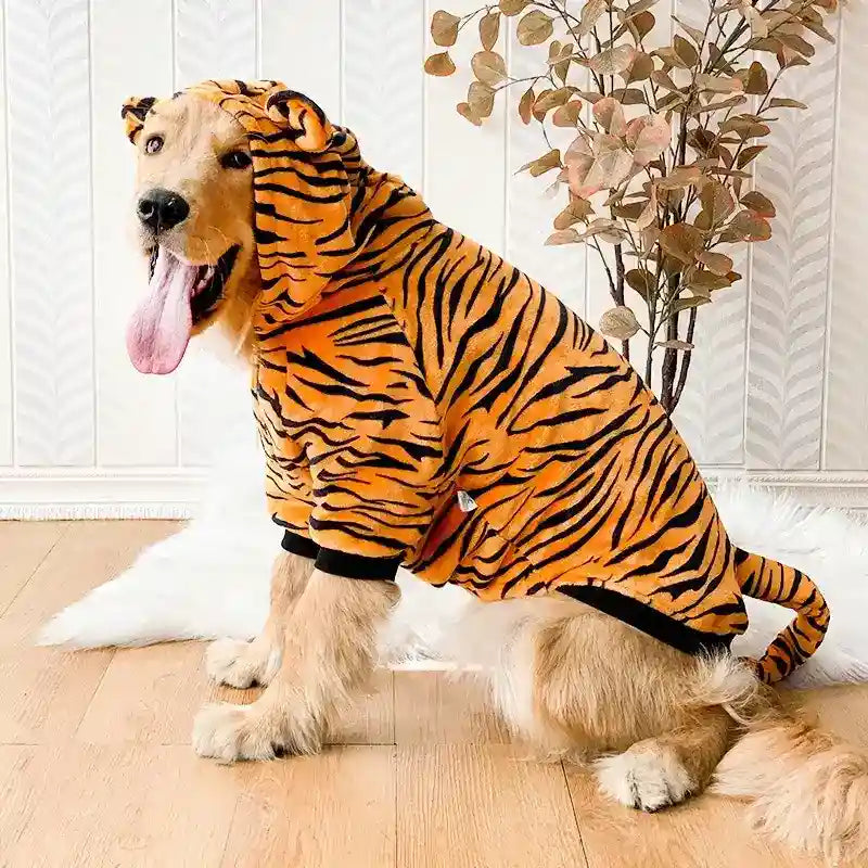 Golden retriever dog wearing orange and black tiger-striped hoodie sitting on wooden floor