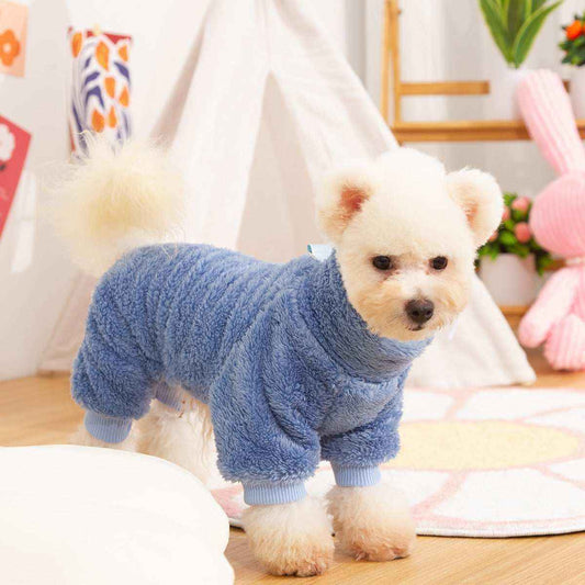 Small white dog wearing cozy blue fleece onesie in bright indoor playroom with toys