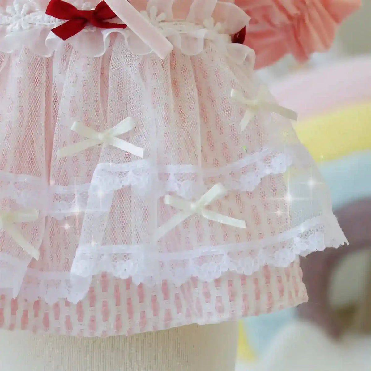 Close-up of pink dress with white lace overlay and small satin bows on fabric