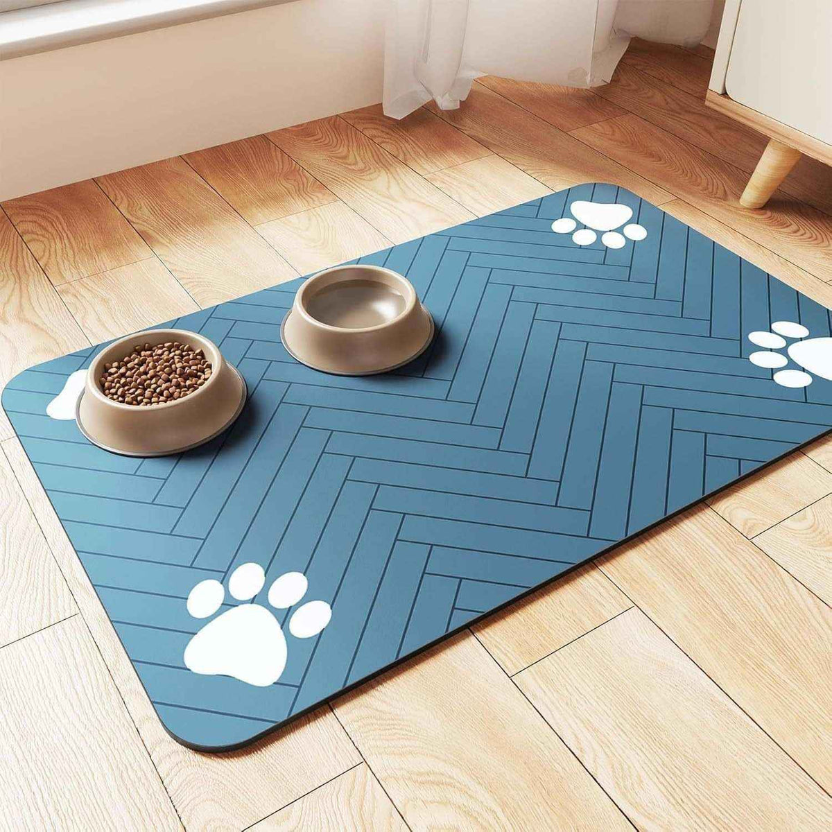 Blue pet feeding mat with white paw prints under two beige bowls on wooden floor
