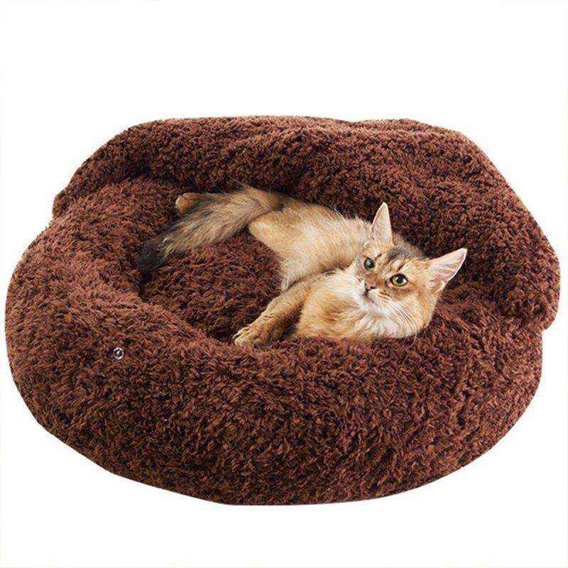 Brown fluffy round pet bed with relaxed cat lying inside on white background