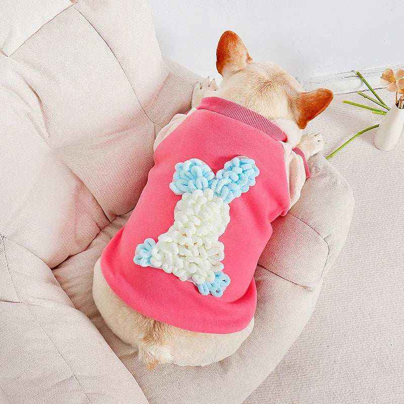 French Bulldog wearing pink sweater with blue and white bunny design lying on beige cushion