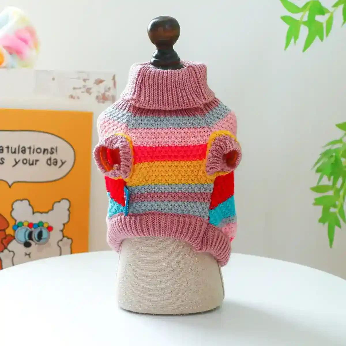 Colorful striped knitted dog sweater on mannequin with pink collar on white table