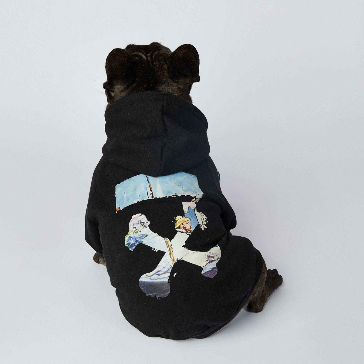 French bulldog wearing black hoodie with artistic white cross and colorful design on back