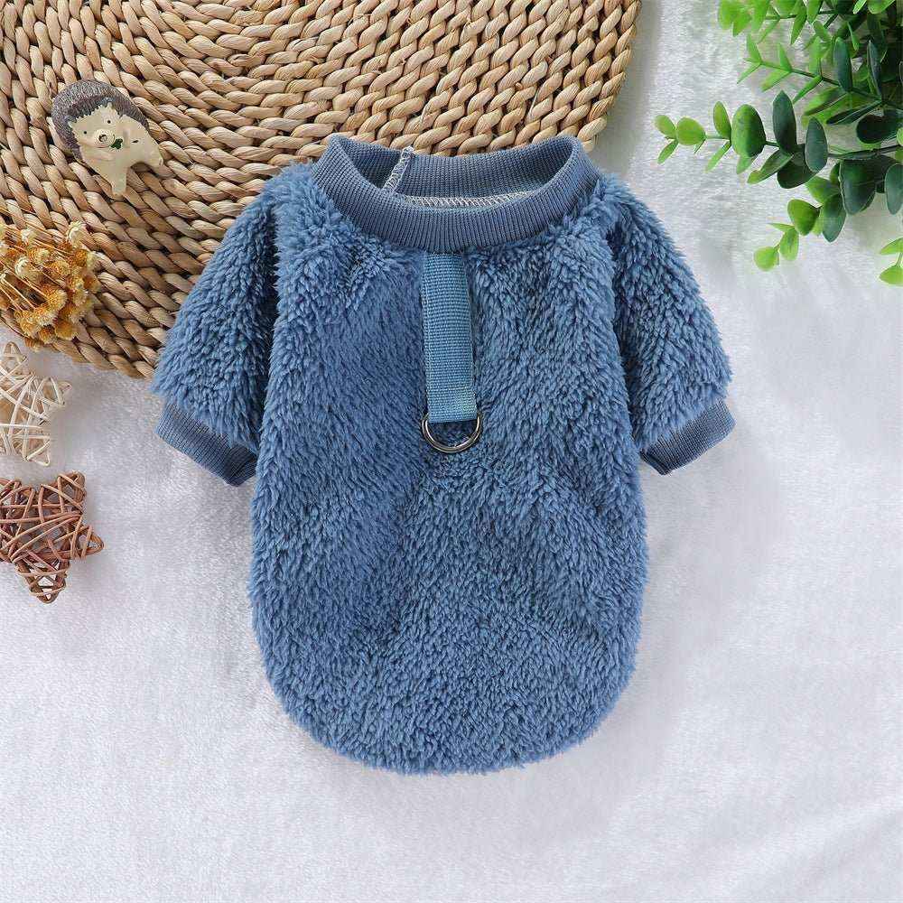 Blue cozy fleece dog sweater with a ring on a white surface with woven placemat and green leaves