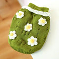 Green knitted pet sweater with white and yellow crocheted flower decorations on wooden floor background