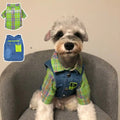 White and gray dog wearing green plaid shirt with denim vest sitting on gray chair