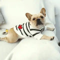 French Bulldog wearing a white and black striped sweater with a red heart, lying on a white couch