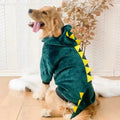 Golden retriever wearing green dinosaur hoodie with yellow spikes sitting indoors on wooden floor