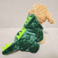 Small dog wearing a green dinosaur costume with spikes and tail on beige couch