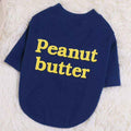 Navy blue pet shirt with yellow text reading 'Peanut butter' laid on a white fluffy surface