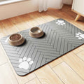 Gray pet feeding mat with white paw prints under two beige pet bowls on wooden floor