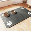 Gray pet feeding mat with white paw prints under two beige pet bowls on wooden floor