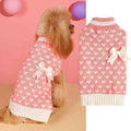 Small dog wearing pink knit sweater with white hearts and bow, displayed beside matching dog sweater