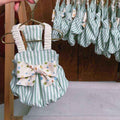 Green and white striped baby romper with multicolor polka dot bow on gold hanger, matching rompers in background