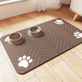Brown pet feeding mat with white paw prints under two beige dog bowls on wood floor