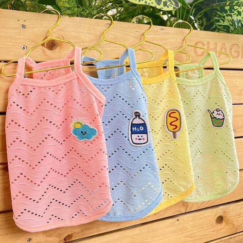 Four colorful breathable dog tank tops with cute patches hanging on gold hangers against wooden background